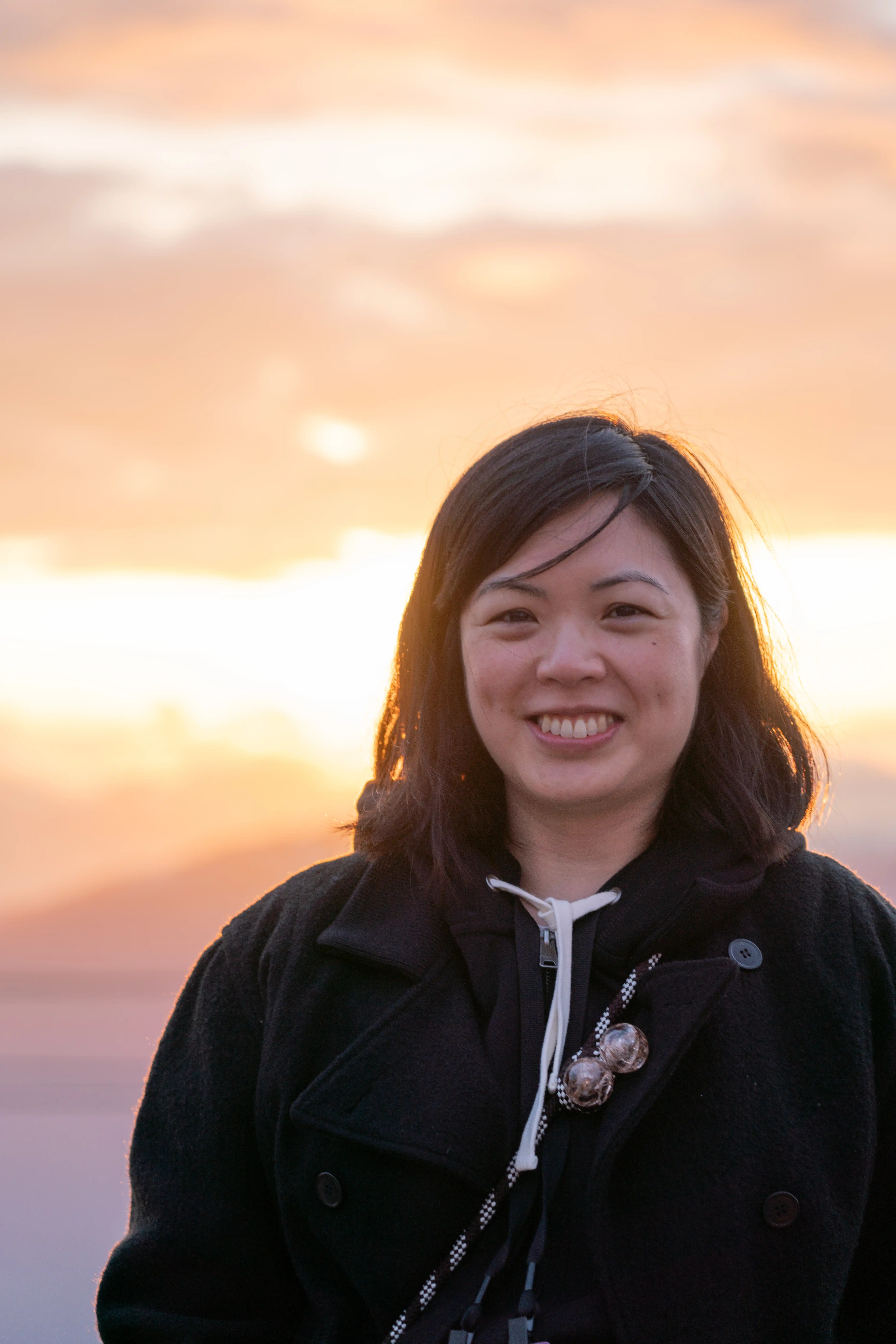 A photo of an Asian woman smiling in front of a light-filled sky